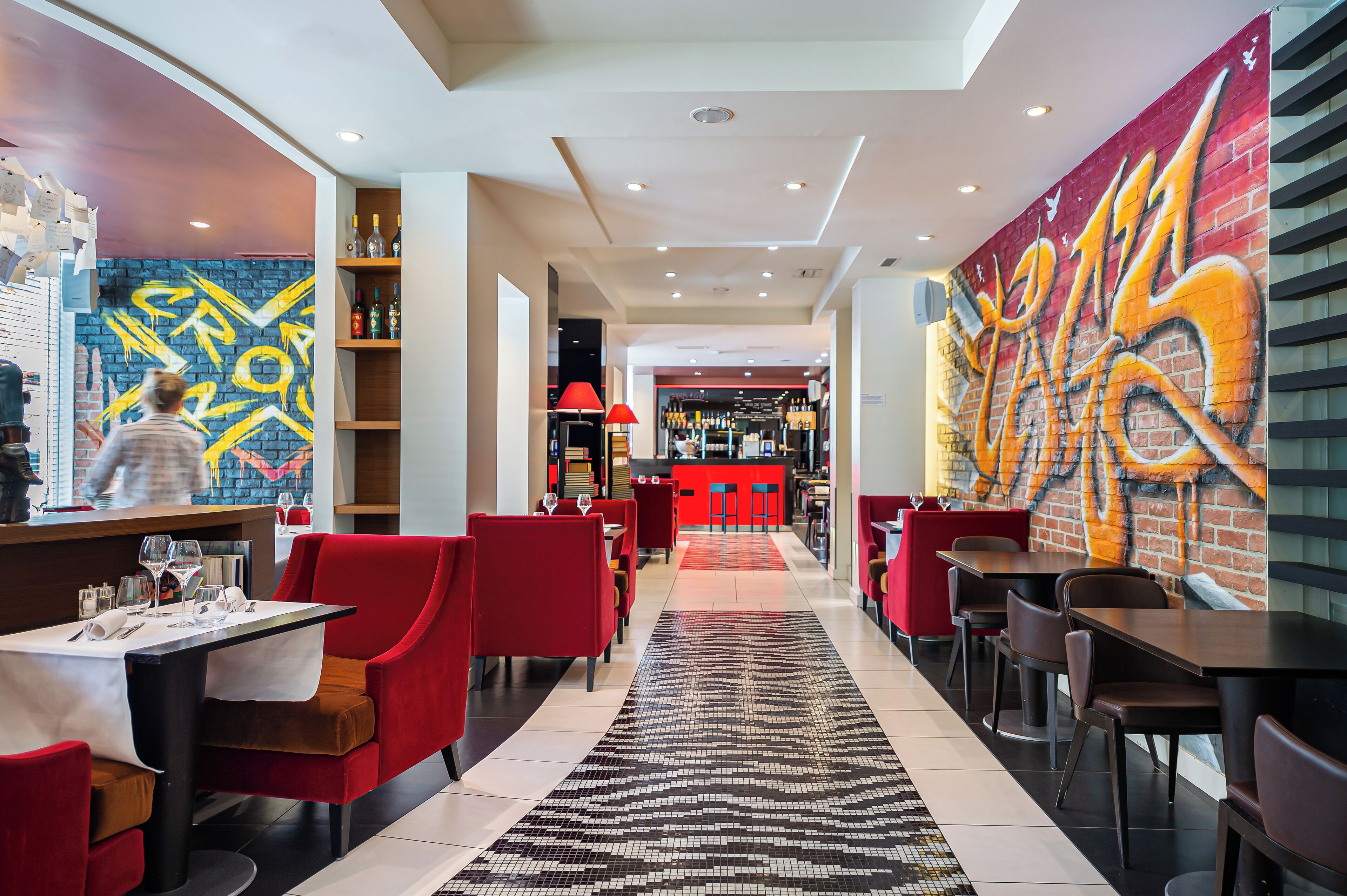 Ein modernes Restaurant mit roten Stühlen, einem schwarz-weißen Teppich und Graffiti-Kunst an den Wänden.