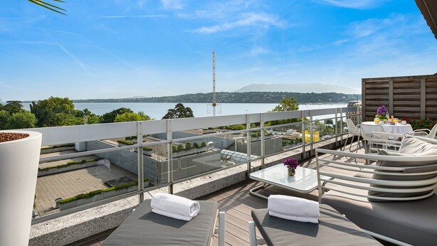 Una terraza en la azotea con mobiliario exterior, una mesa y vistas al mar y a las montañas.