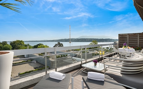 A rooftop terrace with outdoor seating, a table, and a view of the sea and mountains.