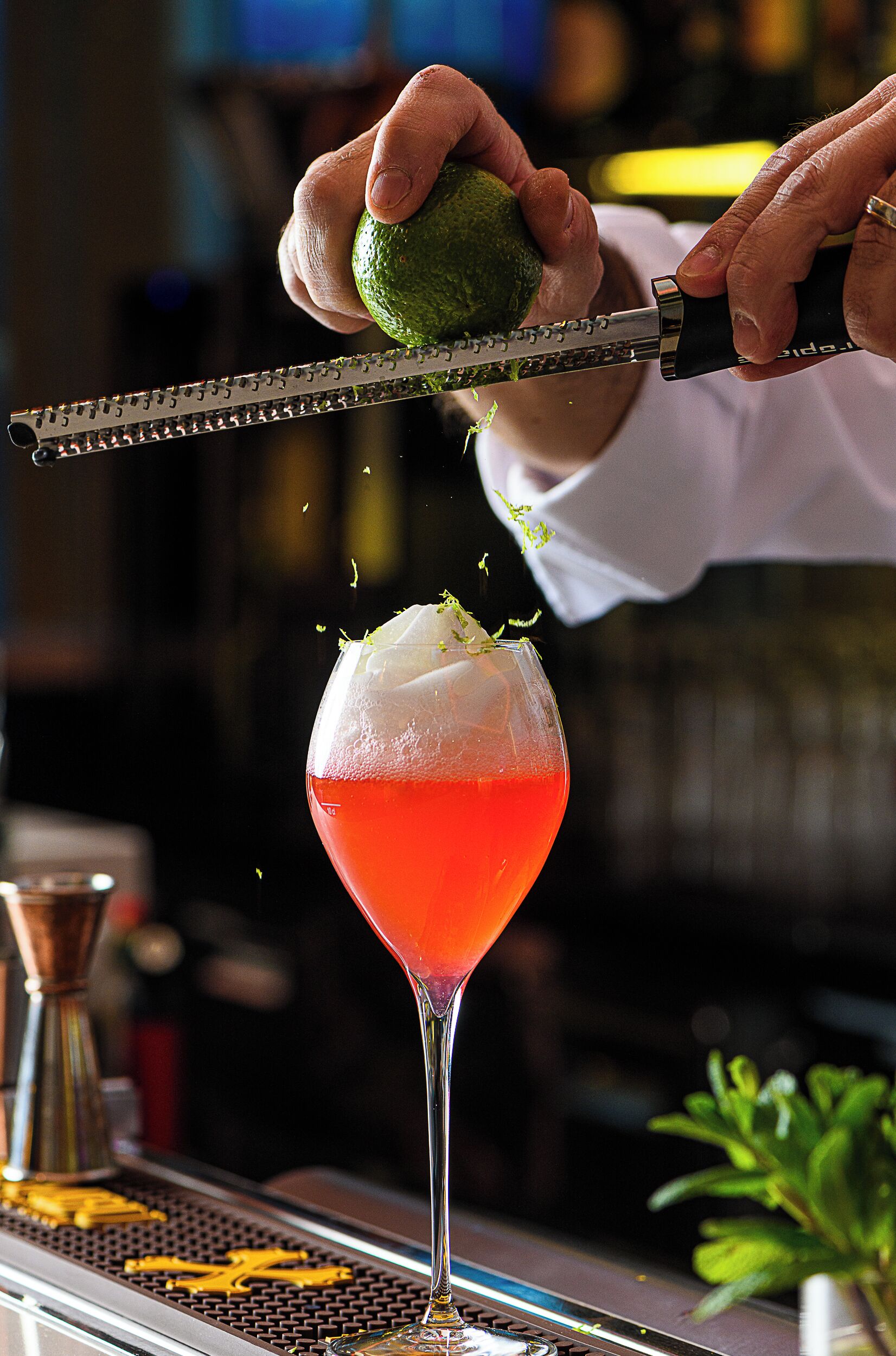 A bartender preparing a cocktail with a lime and a red drink in a martini glass.