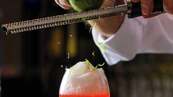 A bartender preparing a cocktail with a lime and a red drink in a martini glass.