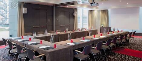 A conference room with a long table, multiple chairs, and a projector screen.