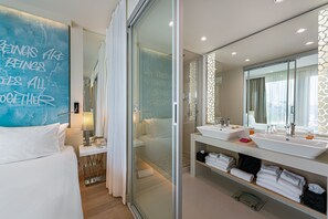 Un baño de hotel moderno con un espejo grande, dos lavabos y una cabina de ducha de vidrio.