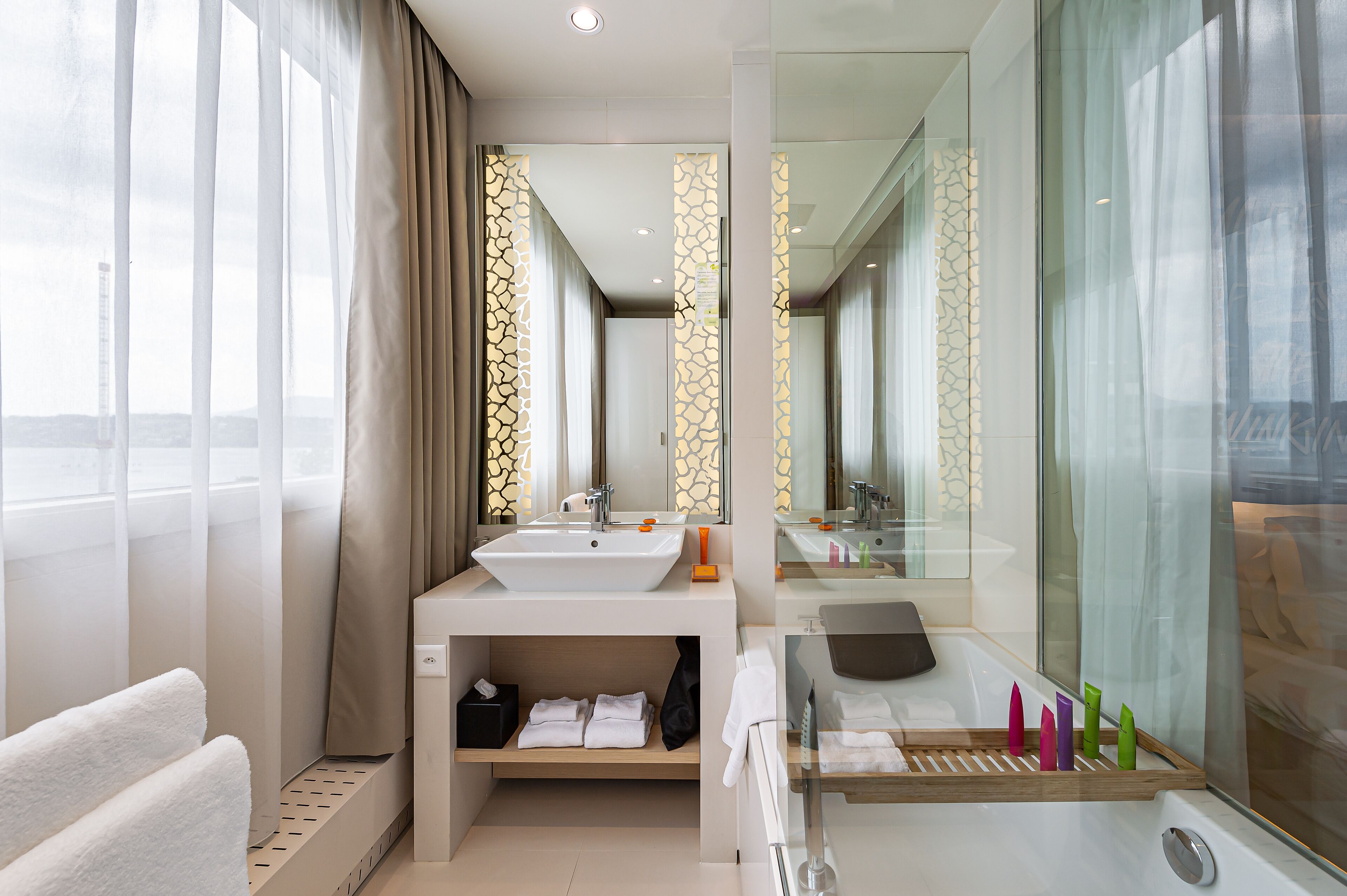 A modern bathroom with a large sink, a bathtub, and a mirror. There are towels and toiletries on the counter.