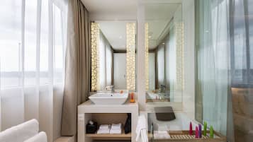 A modern bathroom with a large sink, a bathtub, and a mirror. There are towels and toiletries on the counter.