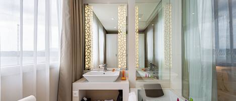 A modern bathroom with a large sink, a bathtub, and a mirror. There are towels and toiletries on the counter.