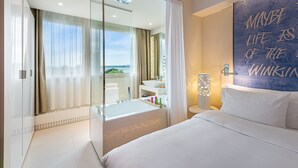 Habitación de hotel moderna con una cama grande, cabina de ducha de vidrio, baño con lavamanos y espejo, y vista a la ciudad.