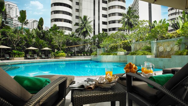 A poolside area with lounge chairs, a table with a fruit bowl and drinks, and a view of tall buildings in the background.