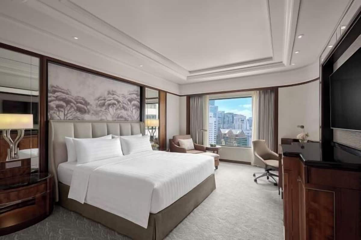 Habitación de hotel con una cama grande, un escritorio, una silla, televisor y vistas a la ciudad.