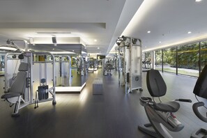 A modern gym with various exercise machines, a bench, and a large window offering a view of greenery. - Shangri-La Kuala Lumpur (Kuala Lumpur)