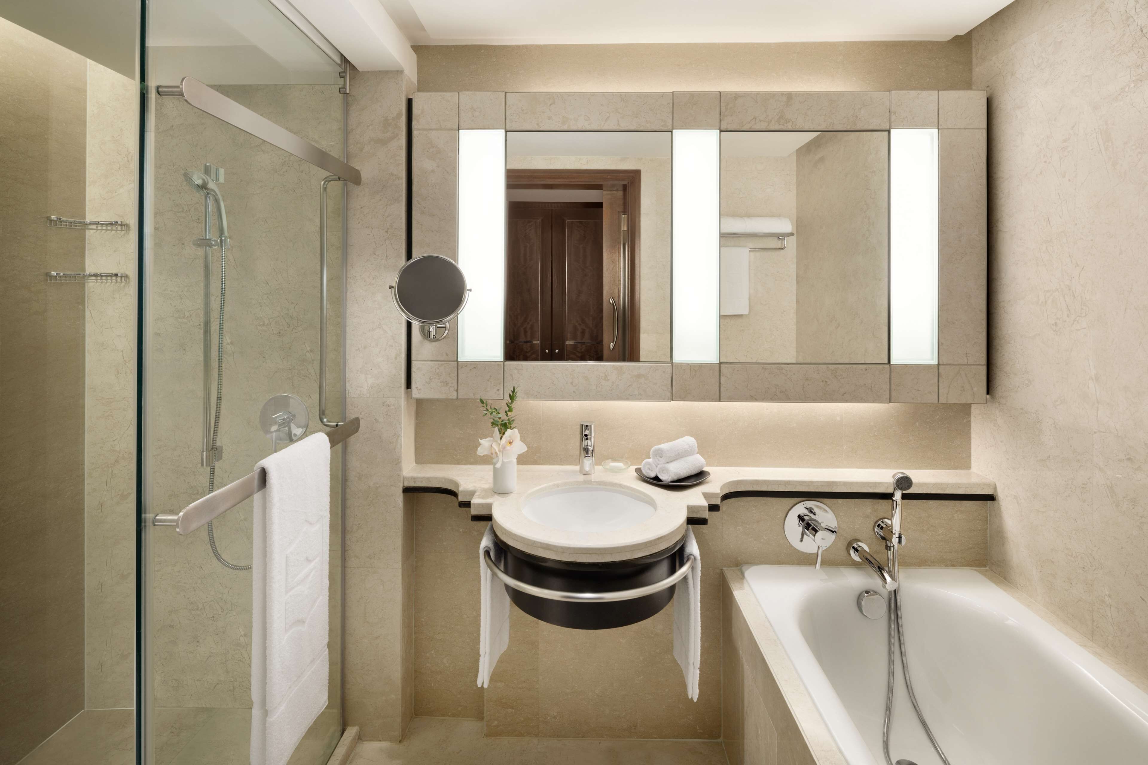 A modern bathroom with a glass-enclosed shower, a round sink with a black sink basin, a large mirror, and a freestanding bathtub.