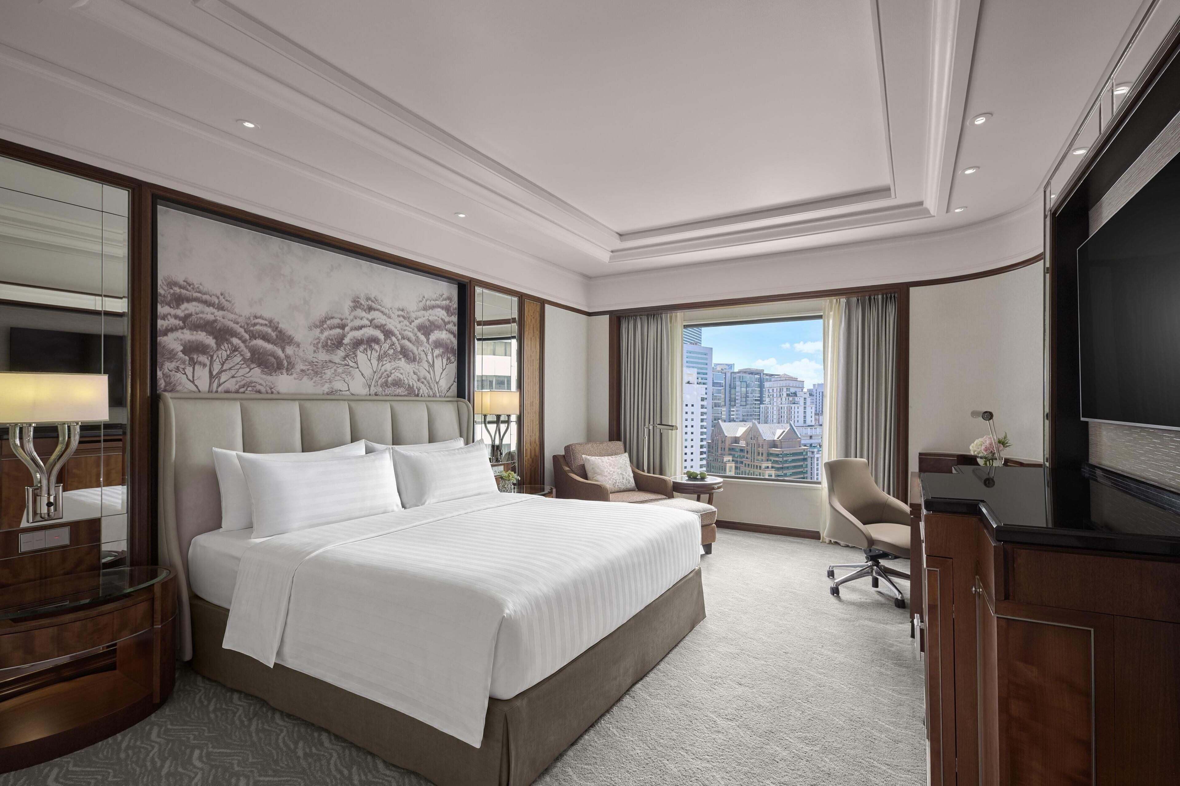 Ein Hotelzimmer mit einem großen Bett, einem Schreibtisch, einem Stuhl, einem Fernseher und Blick auf die Stadt.