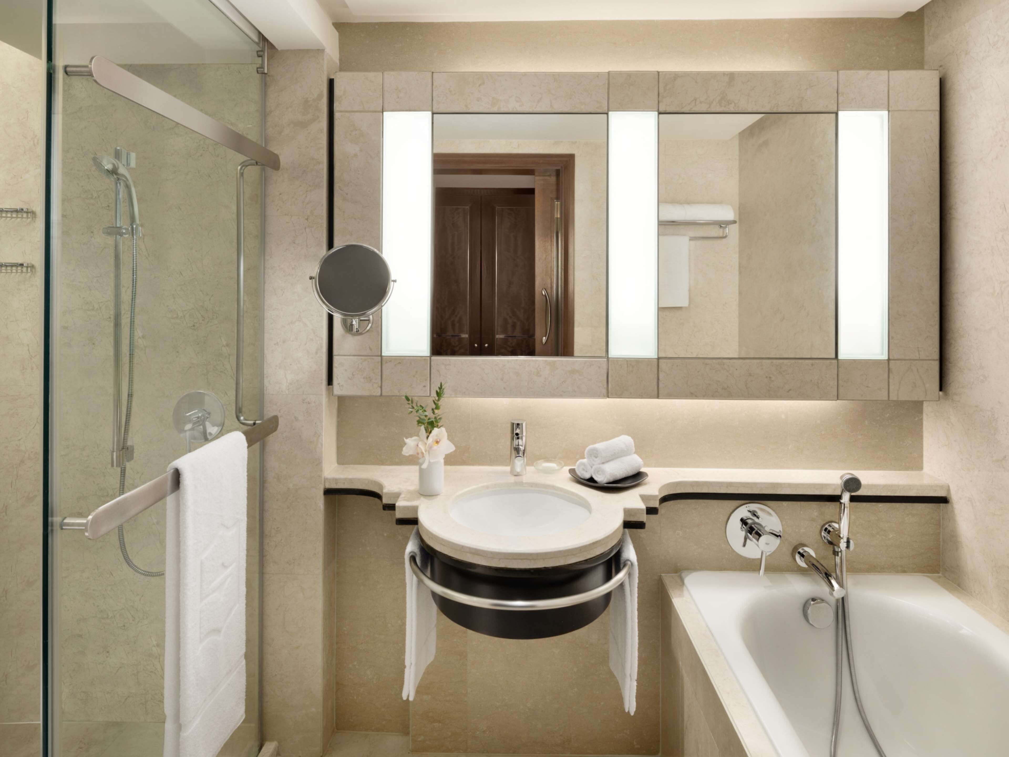A modern bathroom with a glass-enclosed shower, a round mirror, a sink with a black basin, and a bathtub.