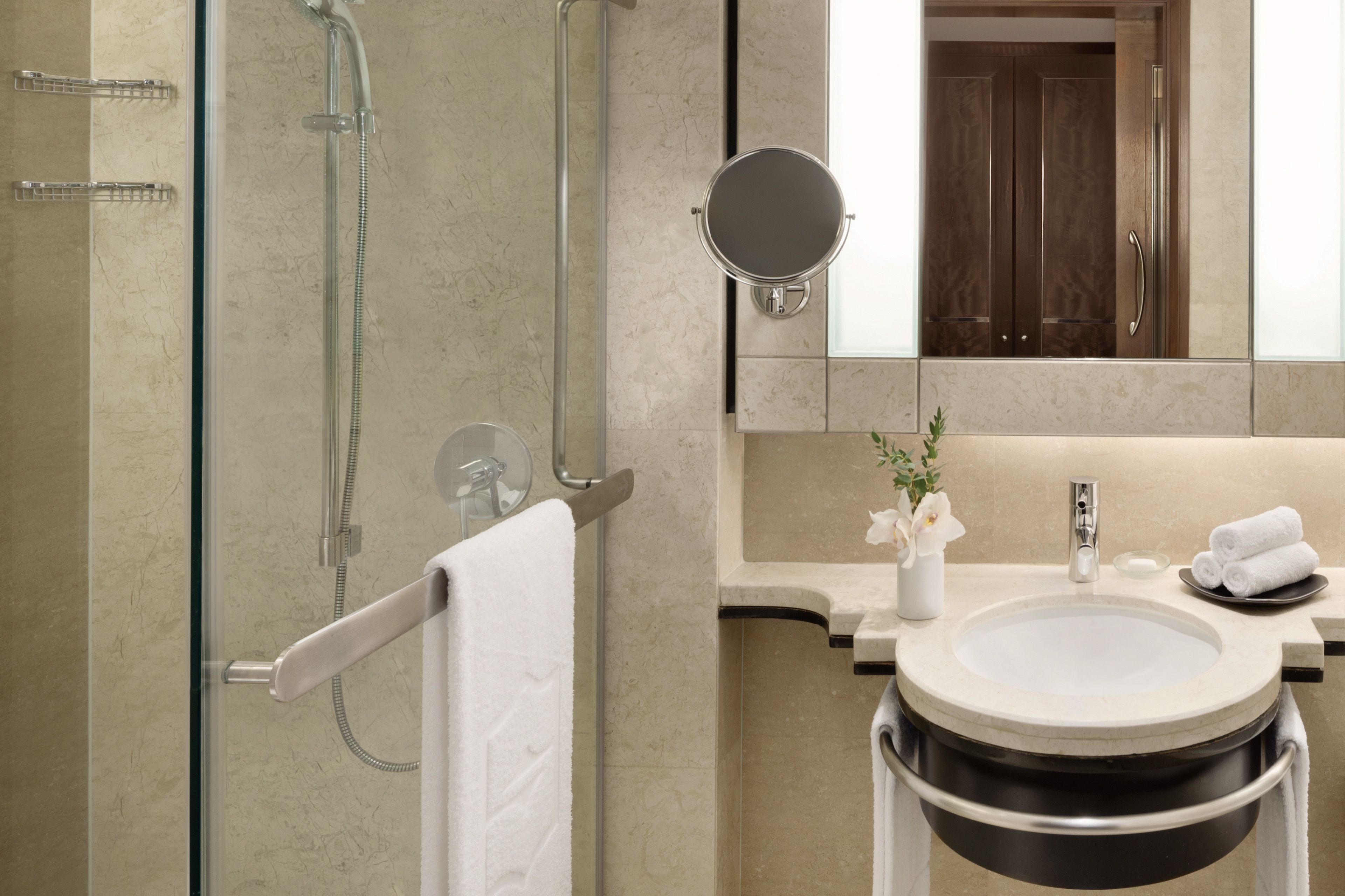 A modern bathroom with a glass-enclosed shower, a round mirror, a sink with a black basin, and a towel rack.