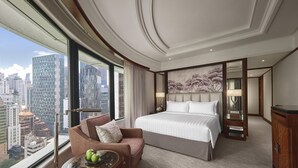A hotel room with a large bed, a sofa, a table with apples, and a city view.
