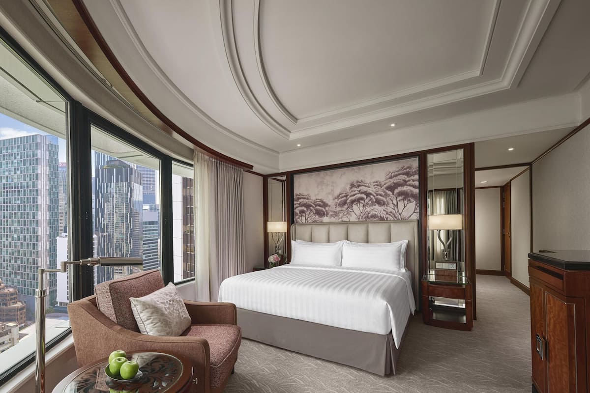 Habitación de hotel con una cama grande, un sofá, una mesa con manzanas y vistas a la ciudad.