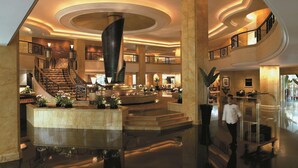A spacious lobby with a grand staircase, a central fountain, and multiple levels with balconies.