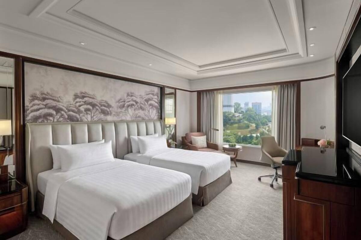 Habitación de hotel con dos camas, un cuadro grande, televisión y vistas a la ciudad.