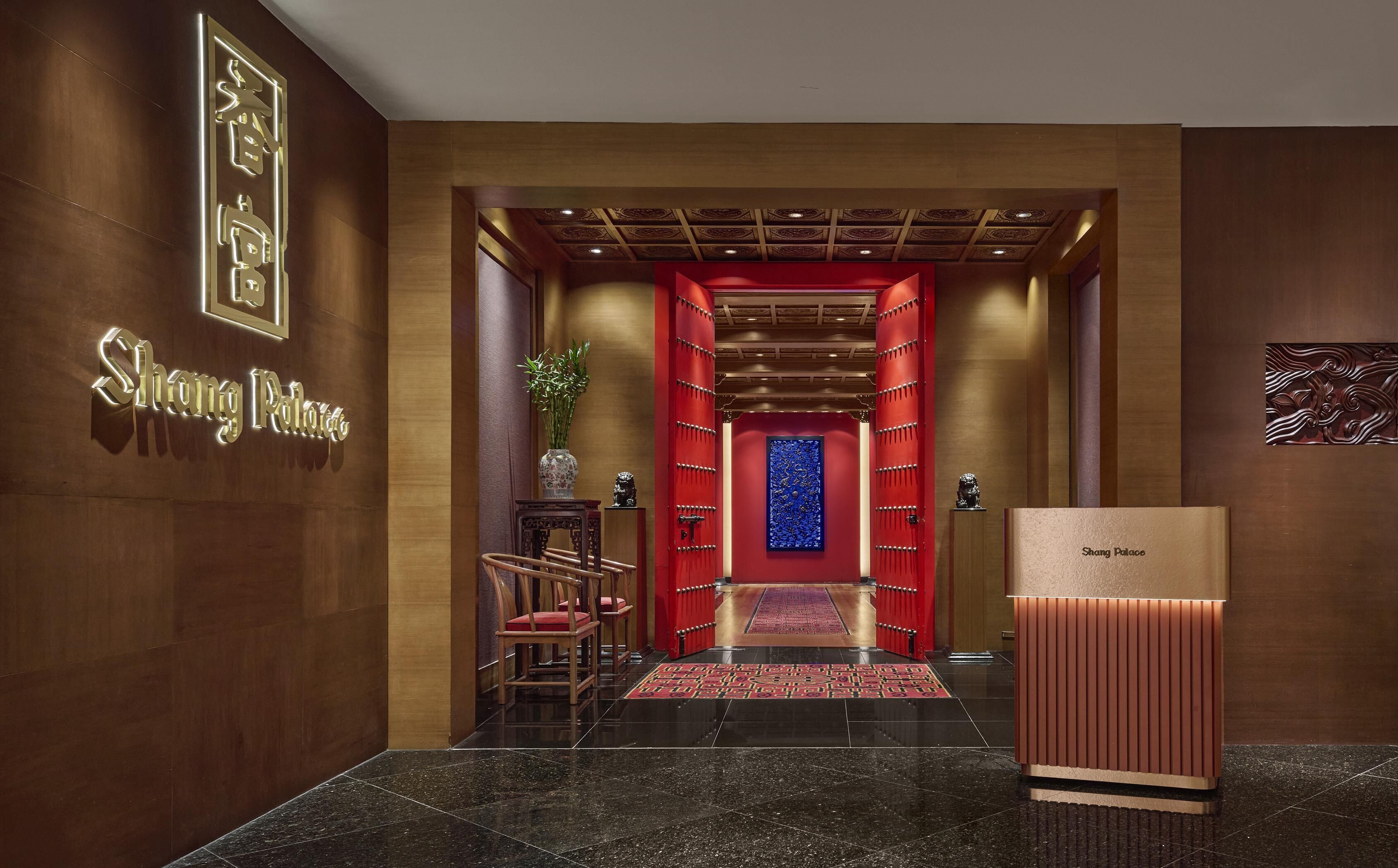 A hotel lobby with a reception desk, a red carpeted area, and a decorative wall with a blue panel.