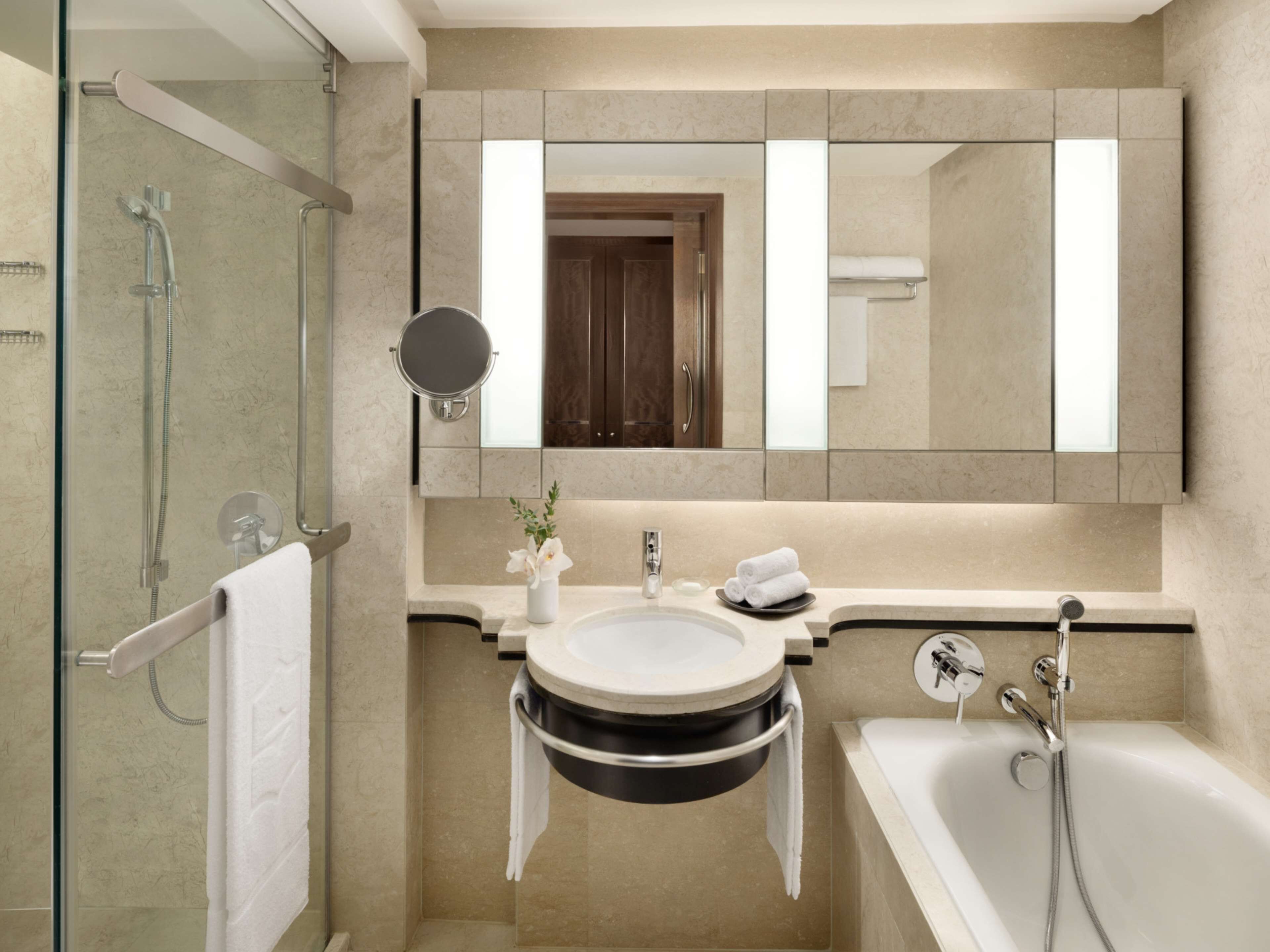 A modern bathroom with a glass-enclosed shower, a round mirror, a sink with a black basin, and a bathtub.