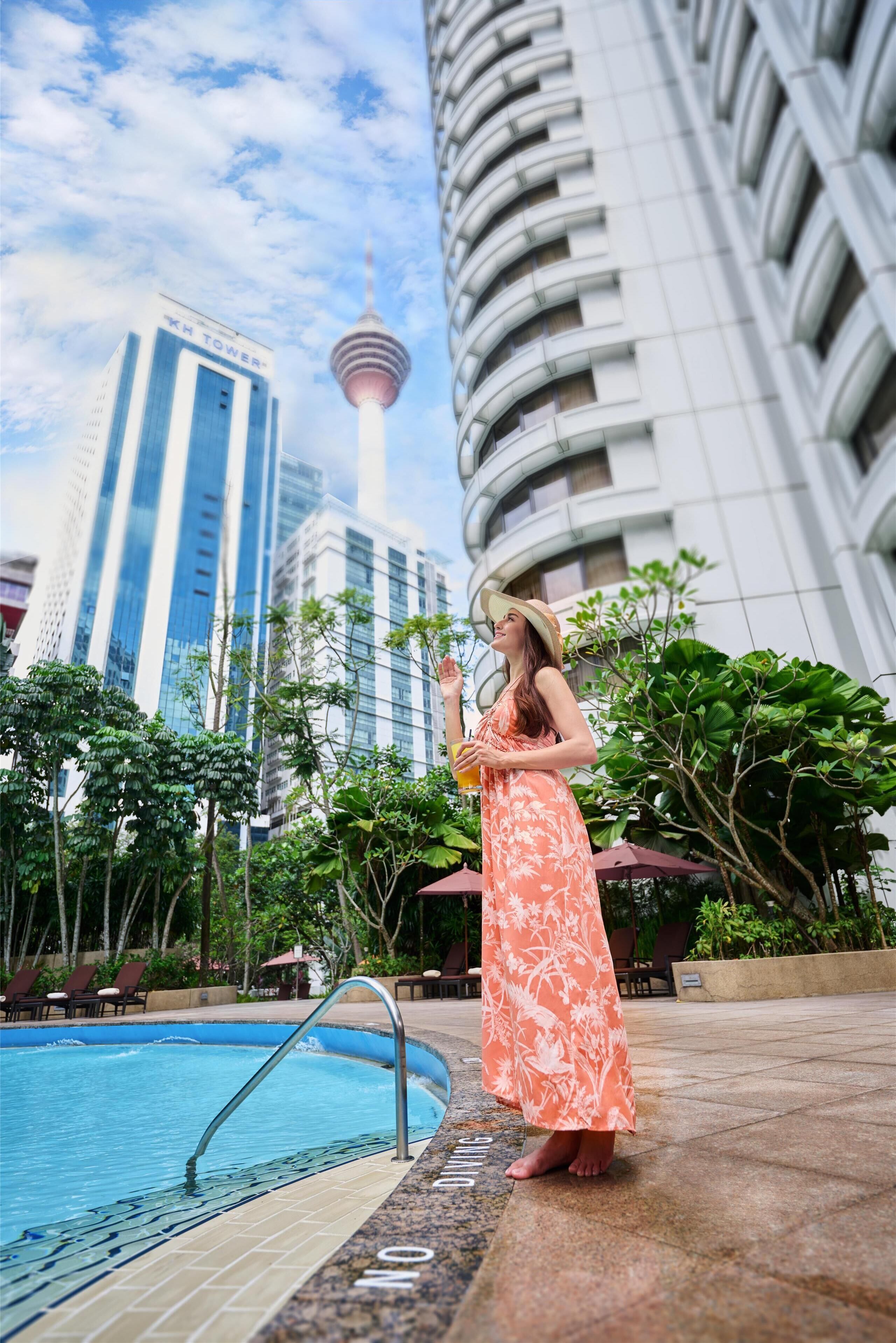 Una persona junto a una piscina con un paisaje urbano de fondo, incluyendo una torre.