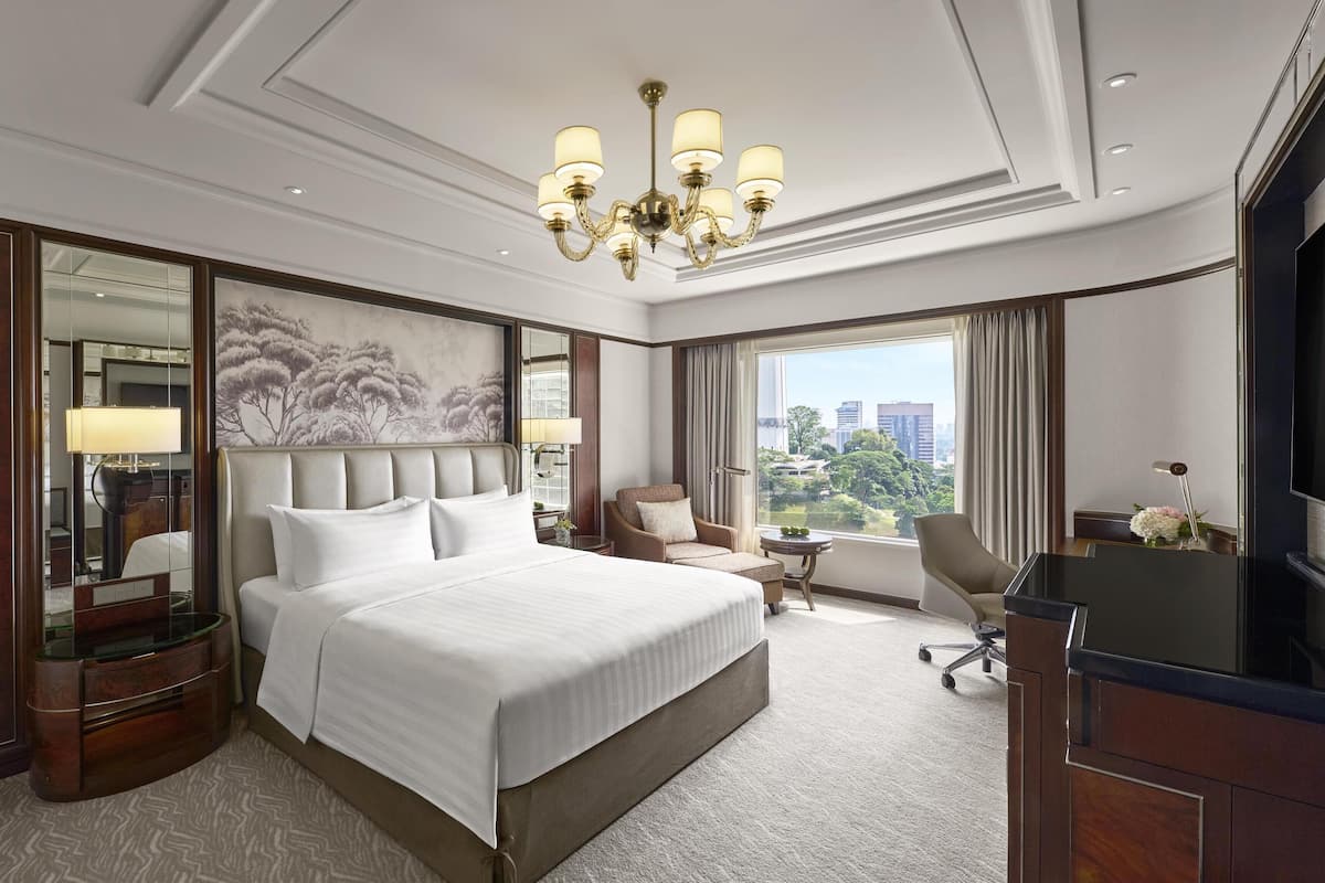 Habitación de hotel con una cama grande, un escritorio con silla, televisor y un ventanal con vista a la ciudad.