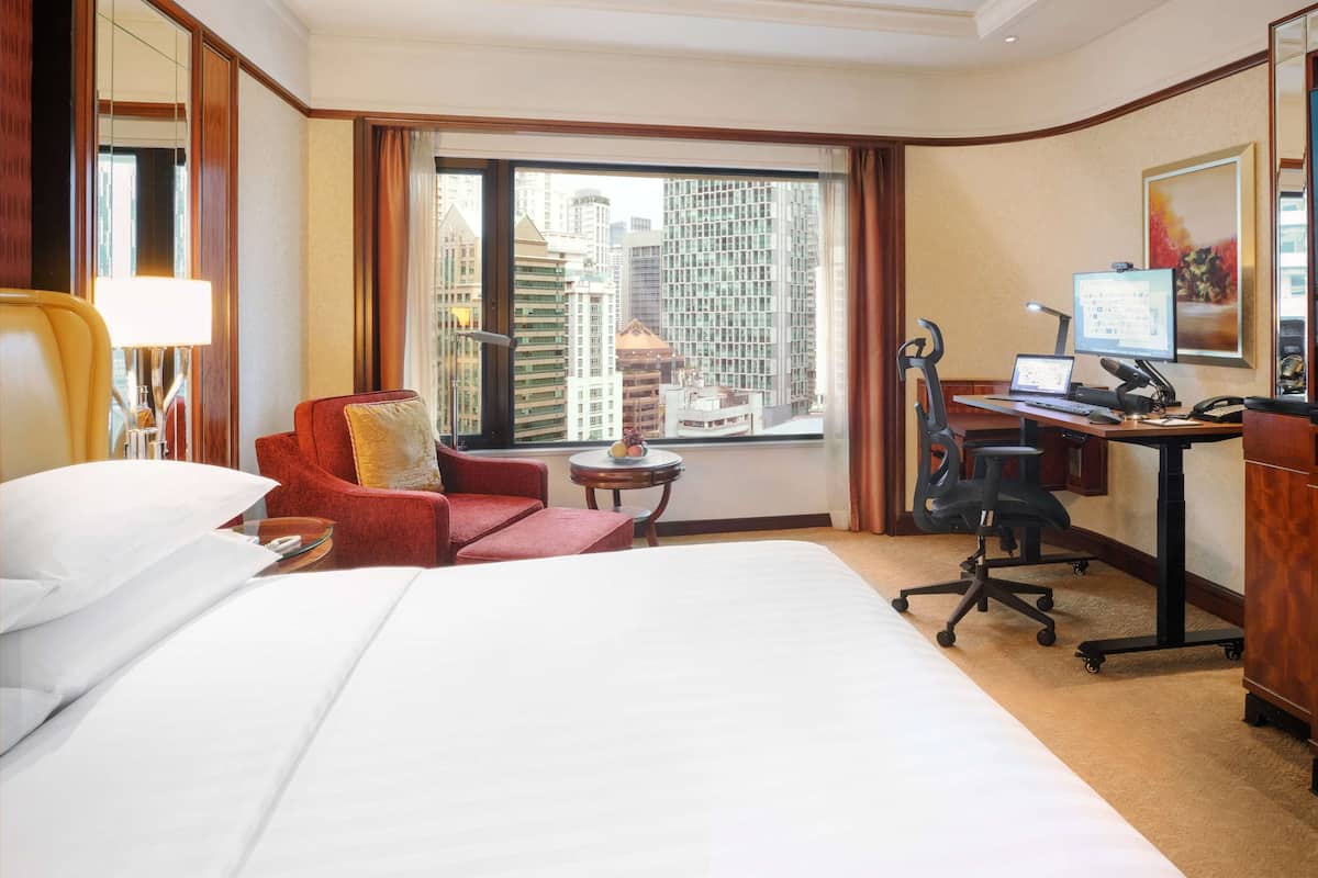 Habitación de hotel con una cama grande, un escritorio con computadora, una silla y vistas a edificios altos.