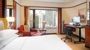 Habitación de hotel con una cama grande, un escritorio con computadora, una silla y vistas a edificios altos.