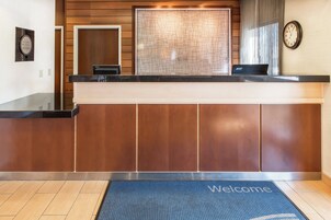 A reception desk with a laptop, a clock, and a welcome mat.