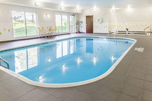 An indoor swimming pool with clear glass walls, a tiled floor, and a door leading outside.