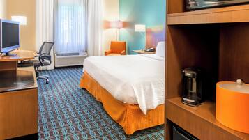 Ein Hotelzimmer mit Bett, Schreibtisch, Stuhl, Klimaanlage, Lampen und einer Kaffeemaschine.