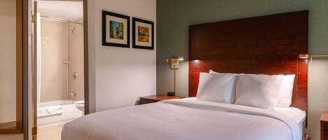 A hotel room with a large bed, a wooden headboard, a nightstand, a wall-mounted lamp, and a framed picture.