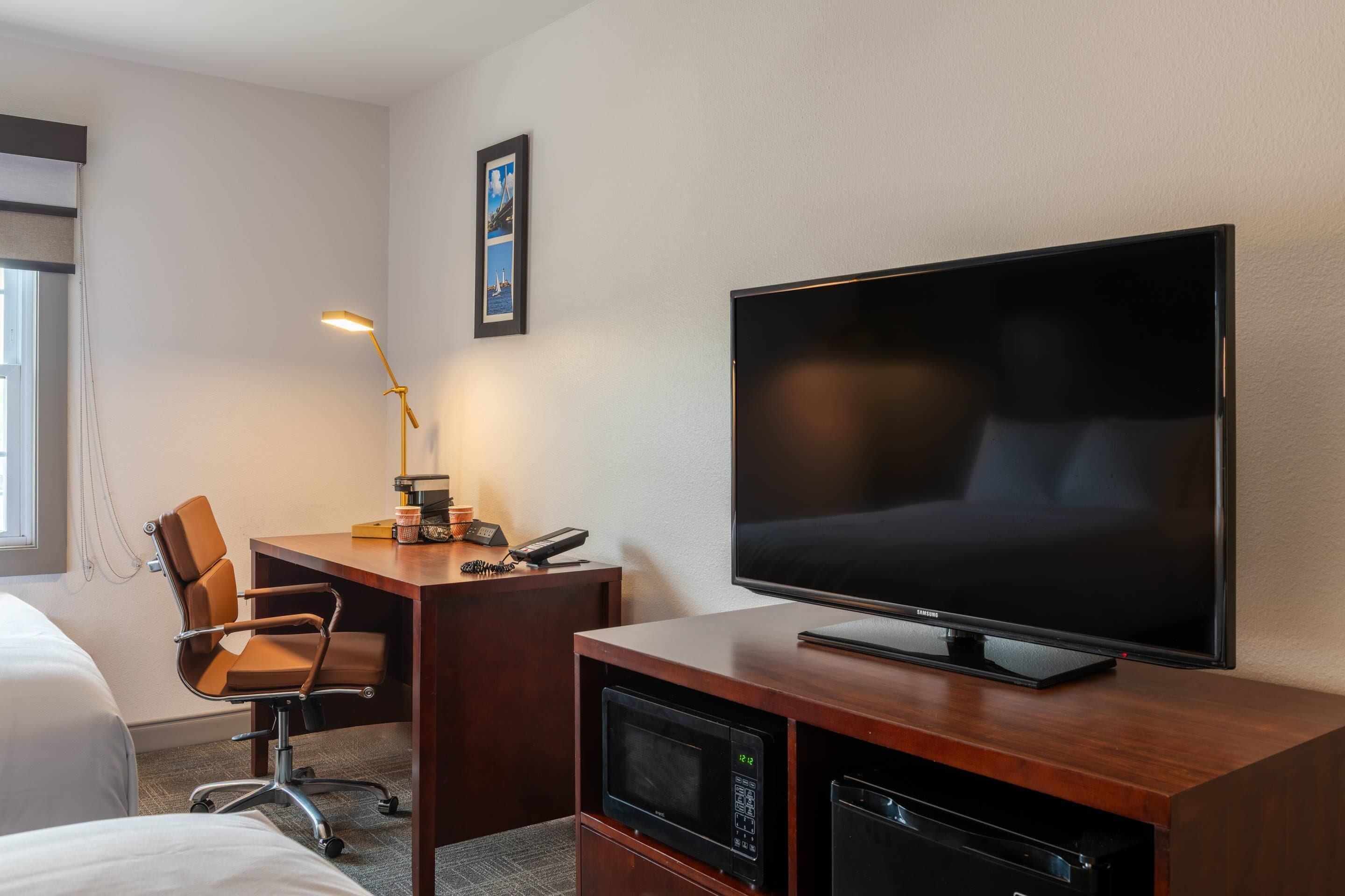 Habitación de hotel con cama, escritorio, silla, televisor y microondas.