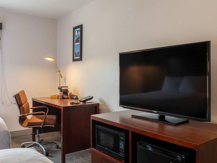 Ett hotellrum med en säng, ett skrivbord med en stol, en tv och en mikrovågsugn.