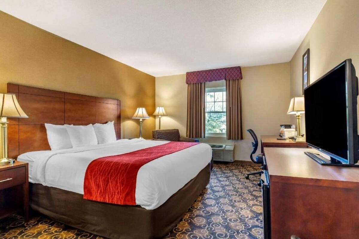 A hotel room with a large bed, two bedside lamps, a television, a desk, and a window with curtains.