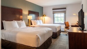 Quarto de hotel com duas camas, uma escrivaninha, uma cadeira, uma televisão e uma janela.