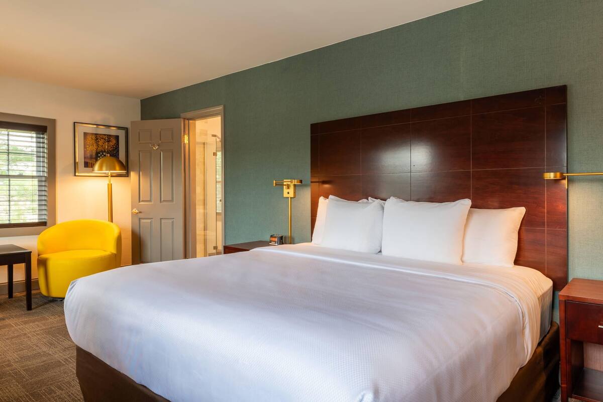 A hotel room with a large bed, a desk, a chair, and a door.