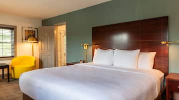 A hotel room with a large bed, a desk, a chair, and a door.