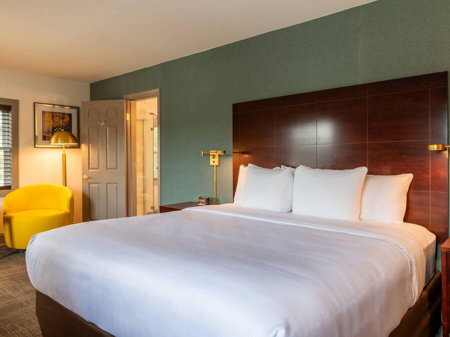 A hotel room with a large bed, a desk, a chair, and a door.