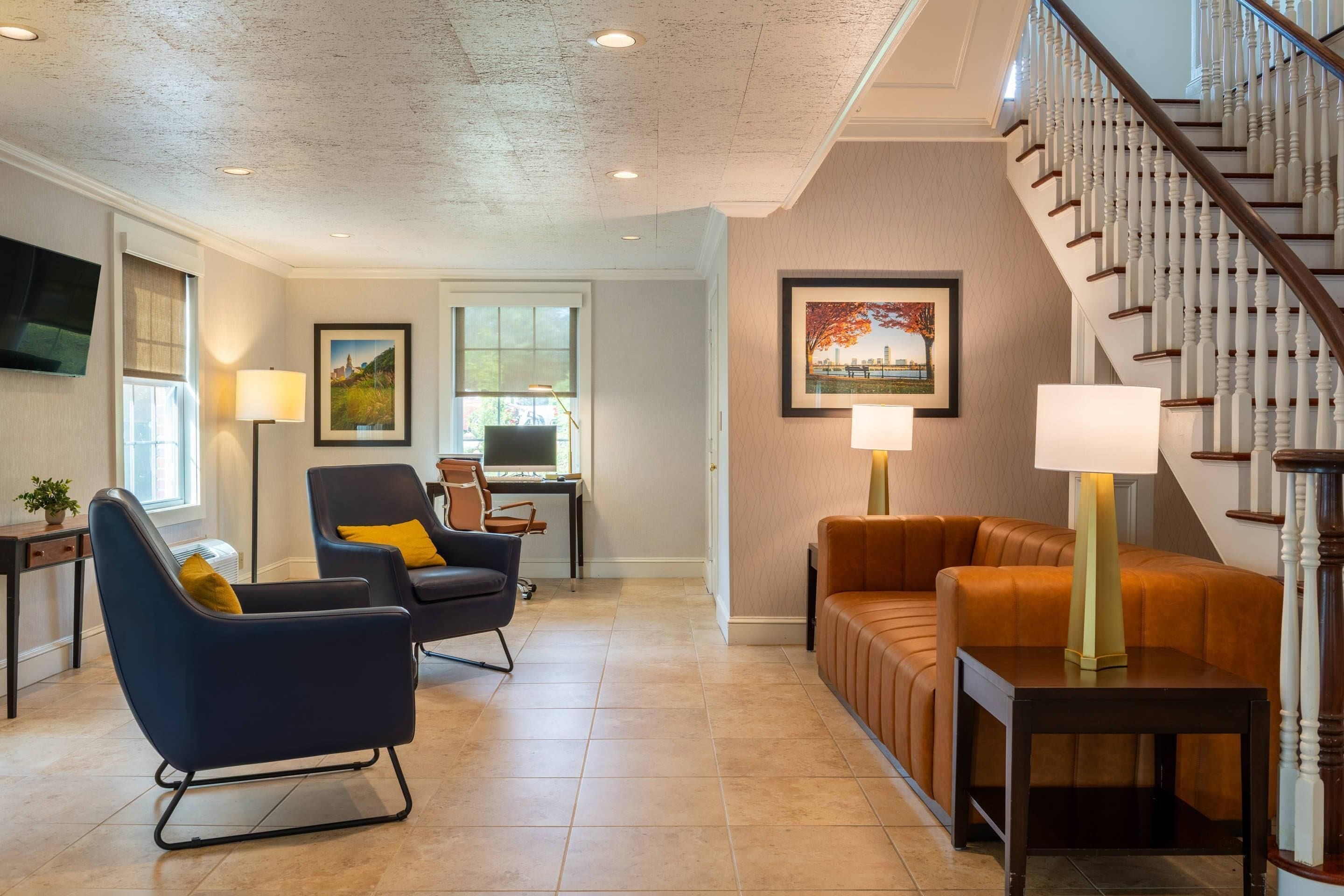 A spacious living room with a modern sofa, a blue armchair, and a wooden coffee table. A staircase with white balusters leads to an upper floor.