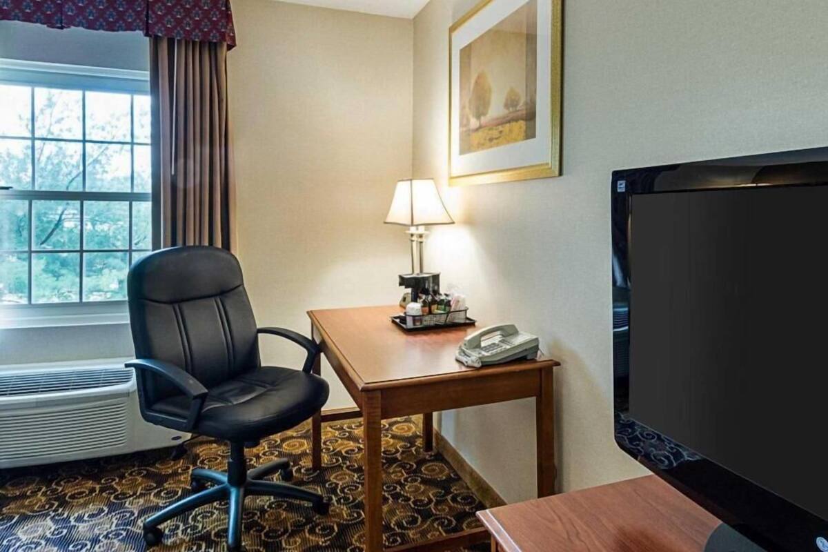 A hotel room with a desk, chair, lamp, telephone, television, and a window with curtains.