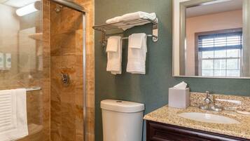 A bathroom with a glass shower enclosure, a toilet, a sink with a mirror, and a towel rack with multiple towels.