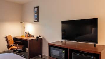 Ein Hotelzimmer mit Bett, Schreibtisch mit Lampe, Fernseher, Mikrowelle und Kühlschrank.