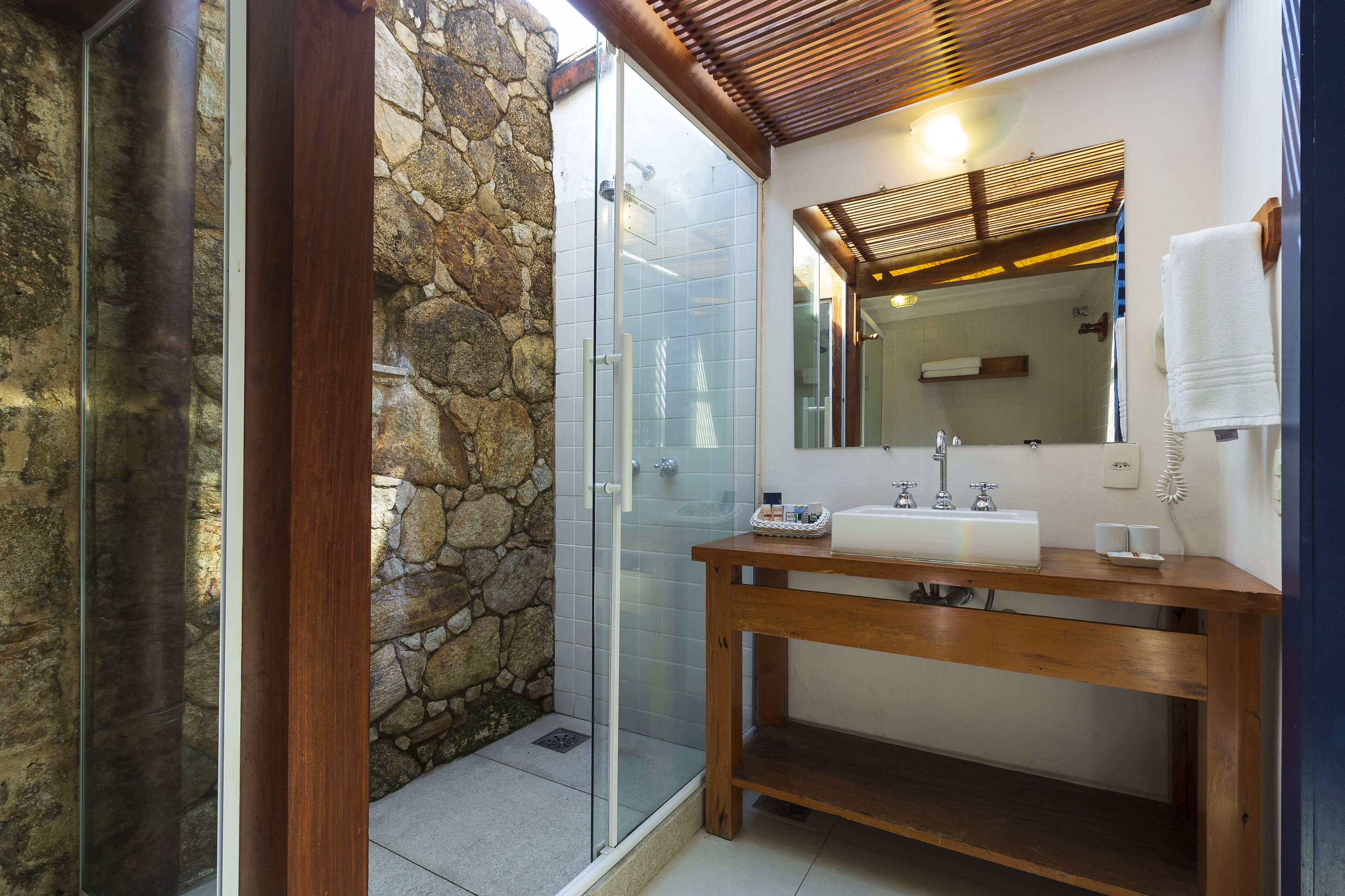 Une salle de bain avec un mur en pierre, une douche en verre, un meuble-lavabo en bois et un miroir.
