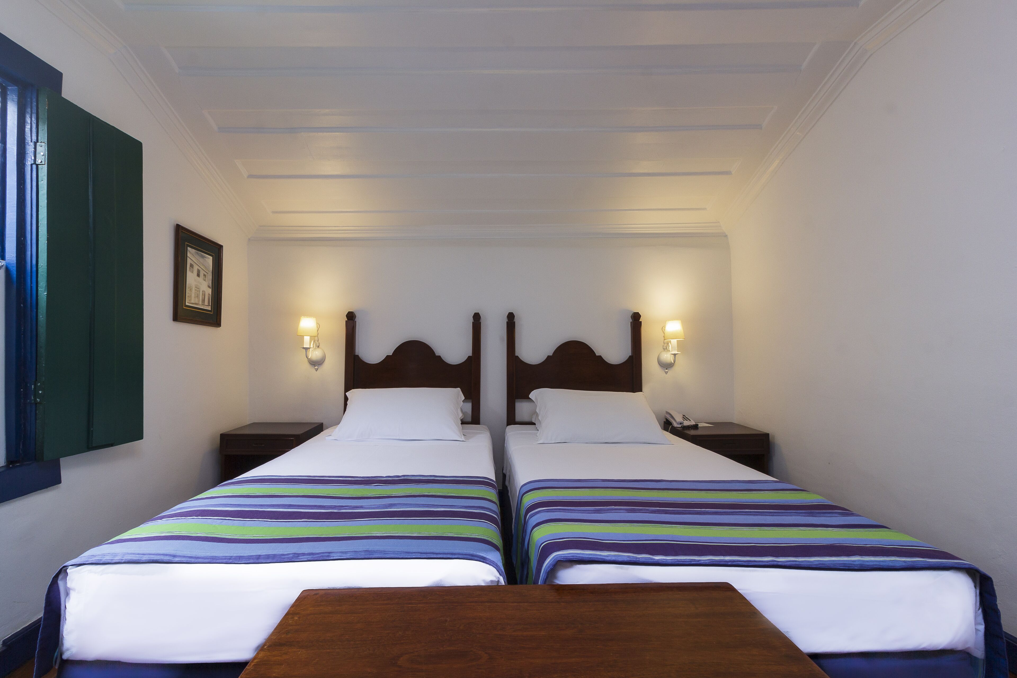 Une chambre d’hôtel avec deux lits, une table en bois et un tableau encadré au mur.
