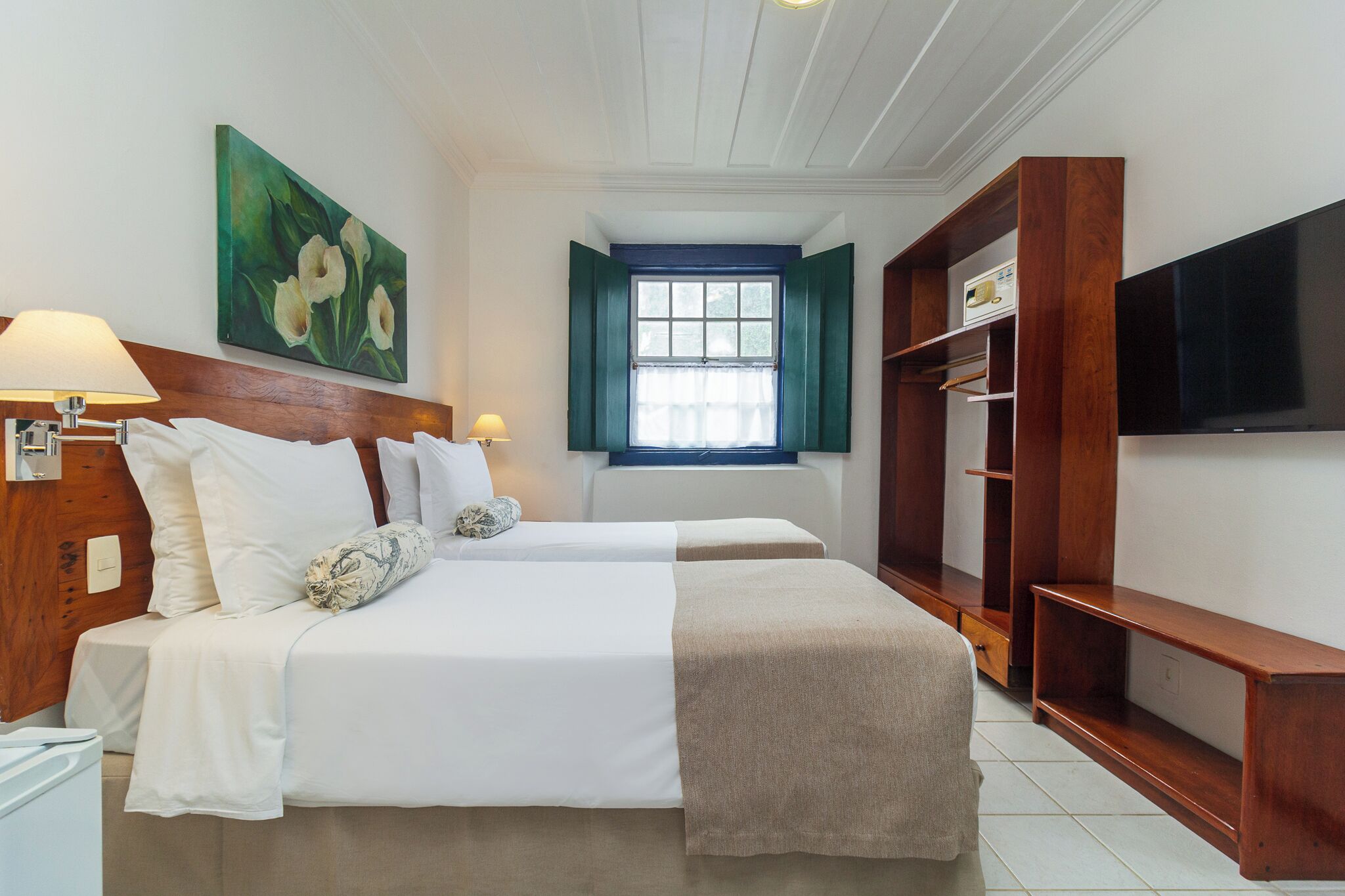 A hotel room with two beds, a TV, a window with shutters, and a wooden wardrobe.