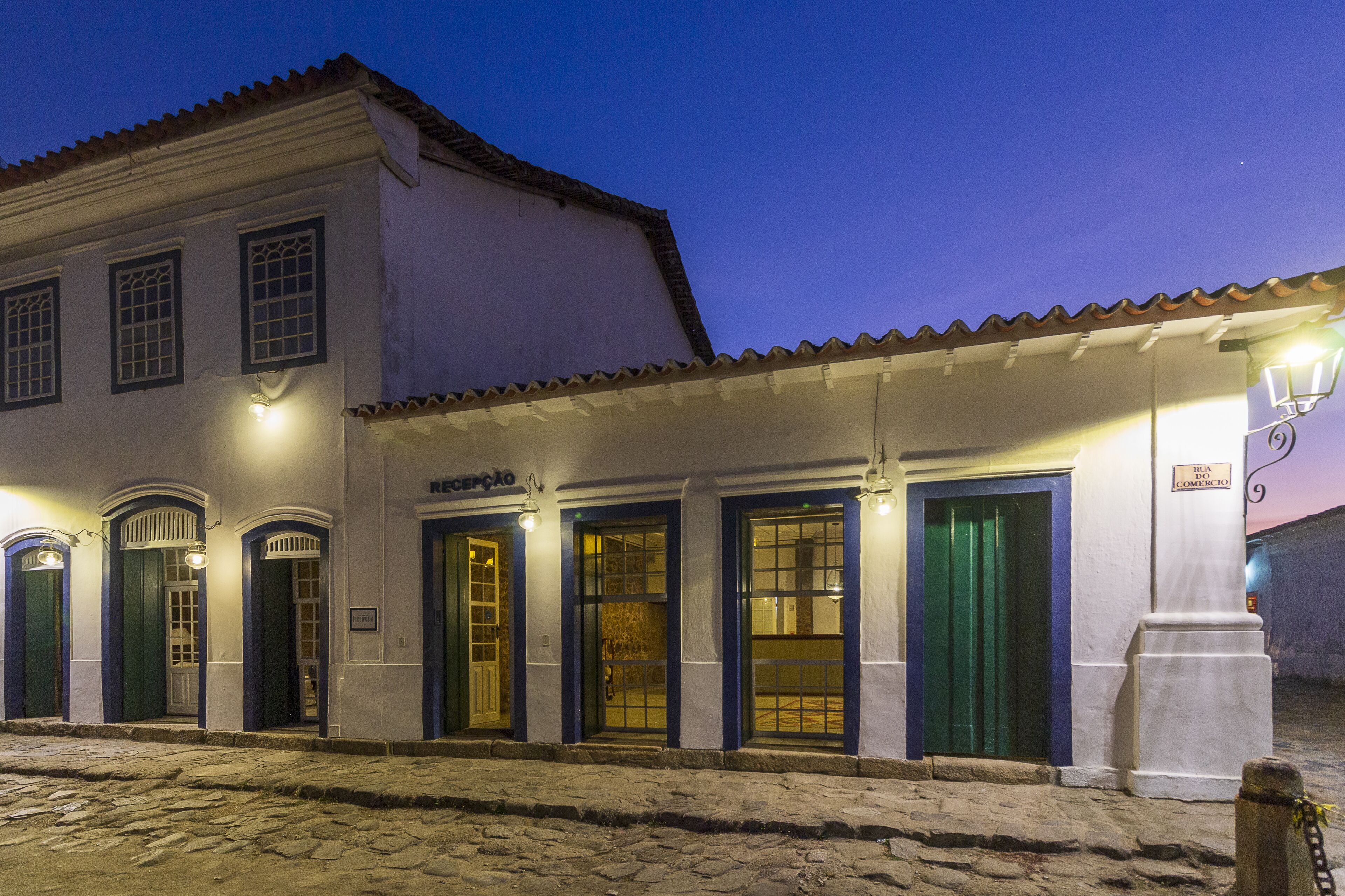 A building with multiple doors and windows, a cobblestone street, and a sign indicating a commercial area.