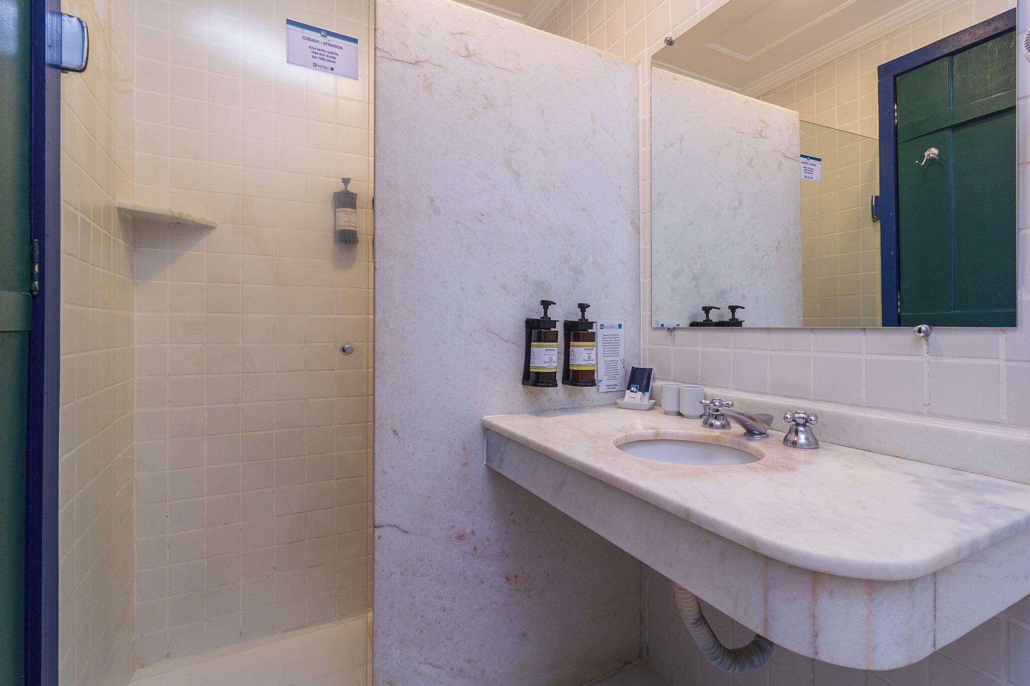 Um banheiro com pia de mármore branco, dois dispensadores de sabonete líquido e uma porta verde.