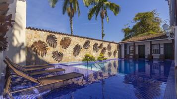 A swimming pool with lounge chairs, palm trees, and a stone wall with leaf patterns.