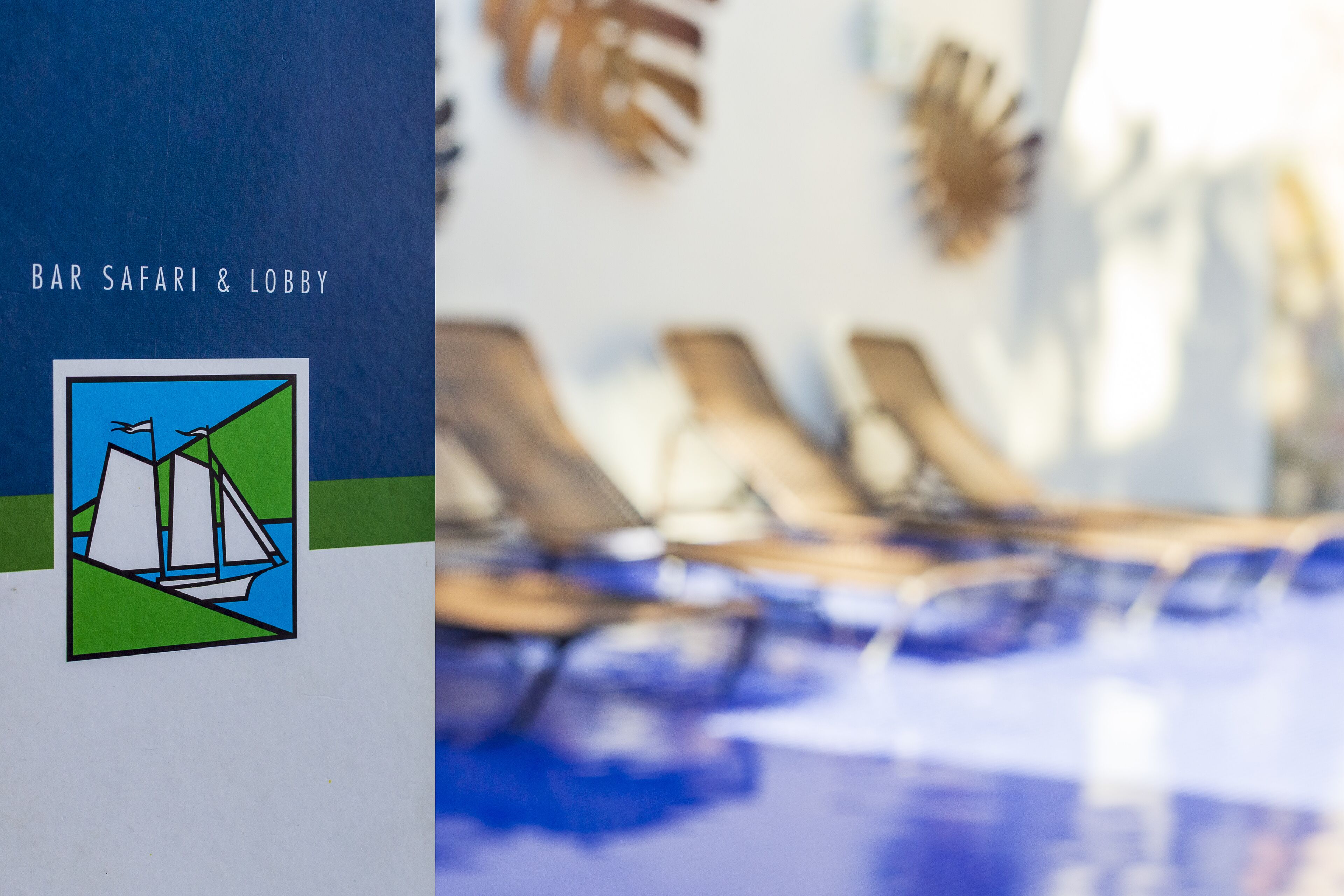 A bar and lobby area with a sailboat logo, lounge chairs, and a pool.